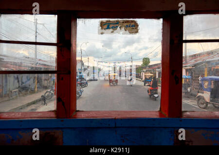 Typical road in Iquitos, Peru, framed by bus window, with motocarros in the background. The rickshaws are the most common form of public transport. Stock Photo