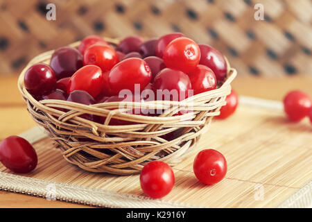 Fresh cornel berries (Cornus mas or Cornelian cherry) in woven basket Stock Photo