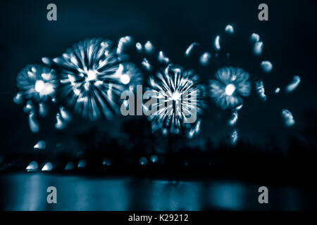 Abstract, blurry, bokeh-style colorful photo of fireworks in a blue tone above the river Stock Photo