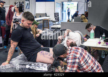 Cornwall Tattoo Convention - a customer watching his upper thigh being tattooed at the Cornwall tattoo Convention Stock Photo - Alamy