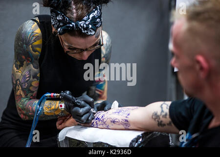 Tattooing. A female tattooist applying a tattoo to the forearm of a customer at the Cornwall tattoo Convention Stock Photo - Alamy