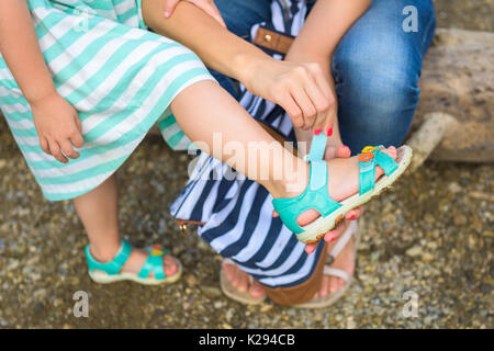 Mother helping her daughter to put on summer sandals Stock Photo