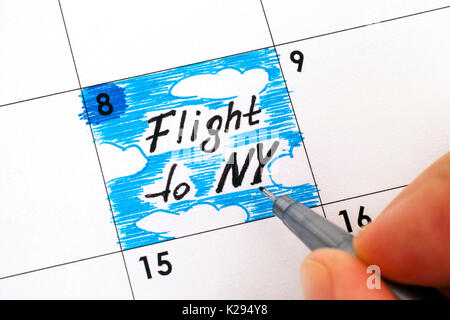 Woman fingers with pen writing reminder Flight to NY in calendar. Close-up. Stock Photo