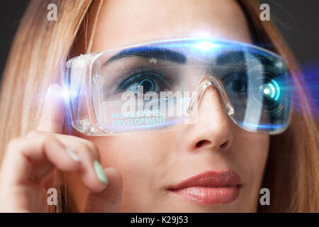 Young businesswoman working in virtual glasses, select the icon mobile apps development on the virtual display. Stock Photo