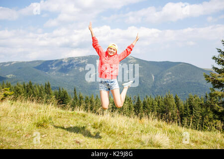 Young teenage girl jumping with raising hands over head in mountains on summer vacation Stock Photo