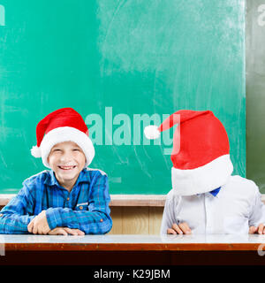 Two boys in santa hats have fun against school blackboard. Christmas concept background with copy space Stock Photo