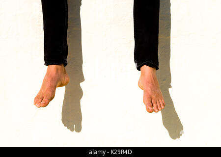Dangling feet casting shadows on a white wall Stock Photo