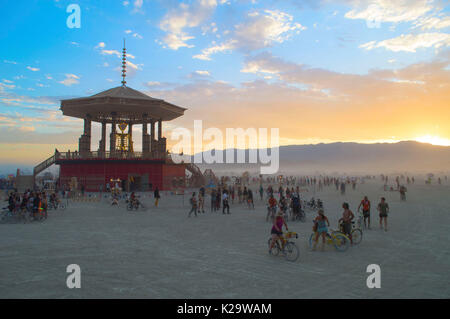 Burners gather around the Burning Man statue at sunset on the playa as the annual desert festival Burning Man closes the first day of the week-long event August 27, 2017 in Black Rock City, Nevada. The annual festival attracts 70,000 attendees in one of the most remote and inhospitable deserts in America. Stock Photo