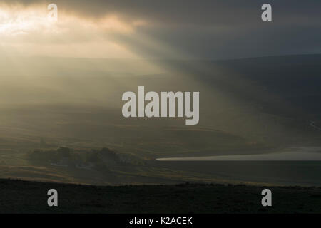 Rays of evening sunlight stream down out of dark clouds over Lower Barden Reservoir & scenic rolling countryside - Wharfedale, Yorkshire, England, UK. Stock Photo