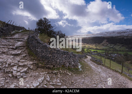 Under blue sky, footpath or stone track, climbs & curves round dry-stone wall, up from Starbotton village, Wharfedale, Yorkshire Dales, England, UK. Stock Photo