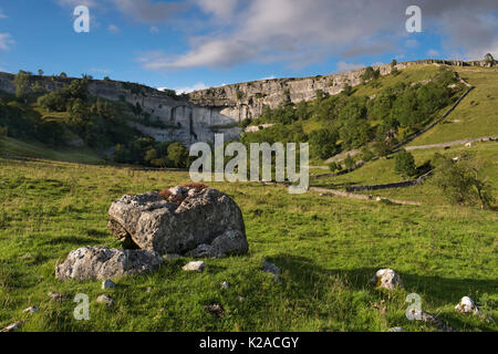 Quiet, sunny, summer evening view of Malham Cove under a blue sky - a huge, curving limestone cliff in the beautiful Yorkshire Dales, England, GB, UK. Stock Photo