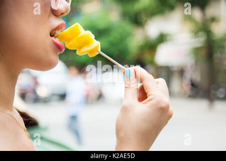 Woman eating pineapple slice from the stick Stock Photo