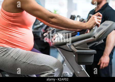 Pregnant woman spinning on fitness bike in the gym Stock Photo