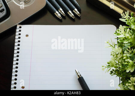 Blank lined paper and pen on wooden desk with phone, flower and the corner of a gold desk lamp. Stock Photo