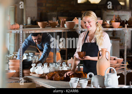 Happy woman in apron carrying ceramic vessels in atelier Stock Photo