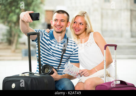 smiling young man holding phone in hands and taking self portrait with girlfriend in city Stock Photo