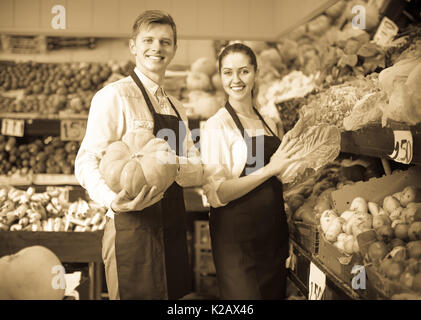 Smiling market stuff offering large squash at the fruit market. Focus on man Stock Photo