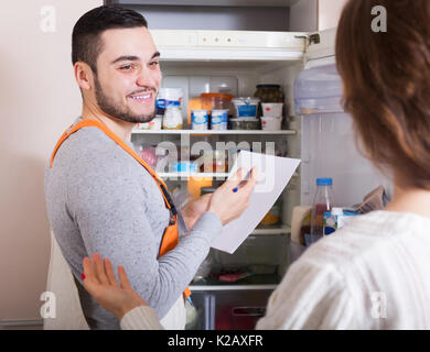 Young housewife showing broken refrigerator to happy repairman Stock Photo