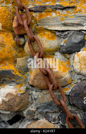 USA Maine ME Monhegan Island an old rusty chain on a rock wall with orange lichen Stock Photo