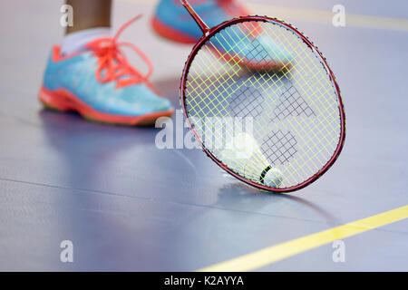 Badminton racket with shuttlecock and player's legs on the court. Stock Photo