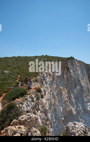 Tourists standing on cliff edge, above Navagio beach on the island of Zakynthos in Greece, taking photographs and selfies. Stock Photo