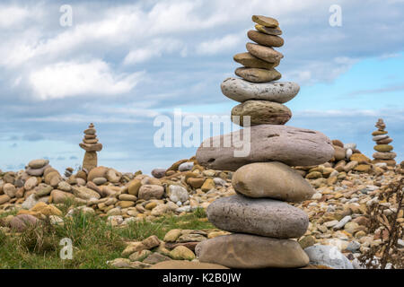 Stone balanced towers of pink and yellow stones, inukshuks or cairns, beach at Holy Island, Lindisfarne, Northumberland, England, UK Stock Photo