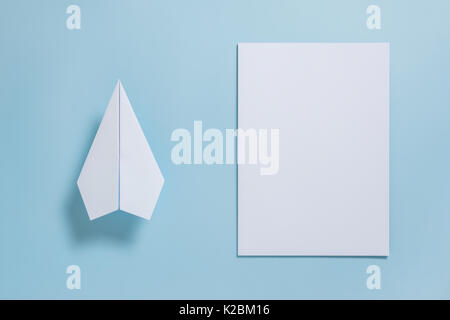 Flat lay of white paper plane and blank paper on pastel blue color background Stock Photo