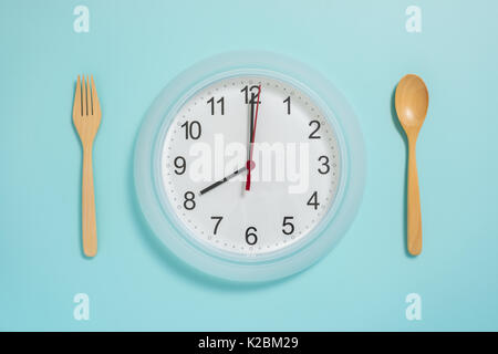 Flat lay of meal time, wall clock spoon and fork on pastel blue color. Stock Photo