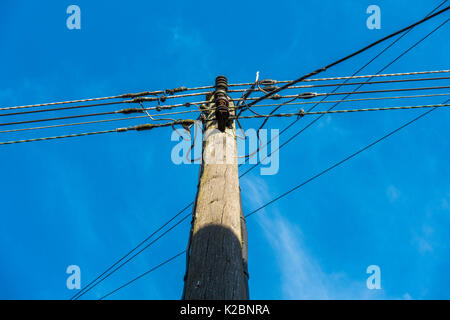 A familiar, traditional, sunlit telegraph pole and telephone cables, viewed from below, against a clear blue sky. Langtoft, Lincolnshire, England, UK. Stock Photo
