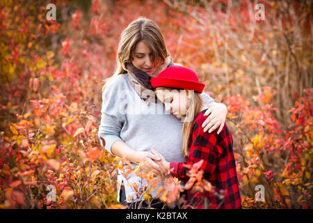 Happy young pregnant mother hugging with teen daughter in autumn park. Happy family concept Stock Photo