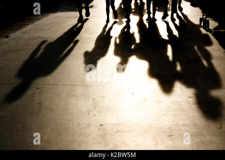 Blurry shadows of people walking towards the camera on seaside promenade in misty summer sunset in black and white Stock Photo