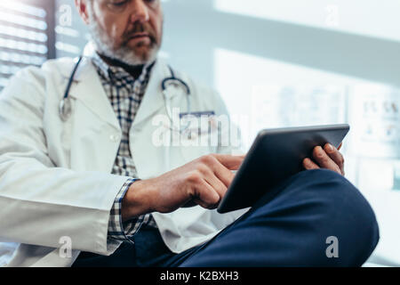 Cropped shot of doctor using digital tablet in his office. Mature male physician sitting at clinic with digital tablet. Stock Photo