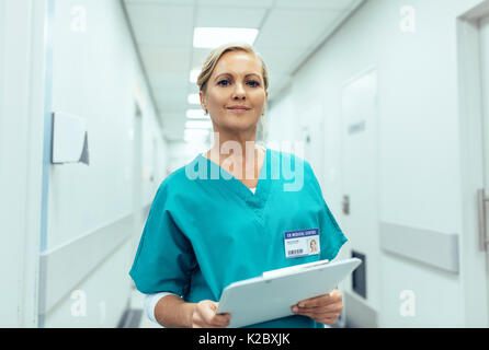 Portrait of mature female nurse working in hospital. Woman healthcare worker with clipboard in corridor.