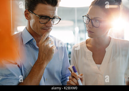 Business colleagues standing behind the glass wall with sticky notes and brainstorming. Business team thinking on new business ideas in office. Stock Photo