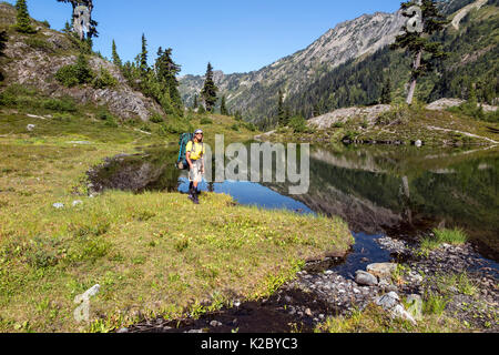 Hiker passing by small lake, Ferry Basin, Bailey Range Traverse, Olympic National Park, Washington, USA, August 2014. Stock Photo