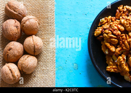 Part of a round wooden plate with shelled walnuts and burlap with the brown nuts on a blue background. Free space for text. Copy space Stock Photo