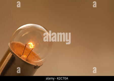 Glowing light bulb on gold brown background. Retro style lamp with ideal spherical surface and filament element. Macro view, copy space