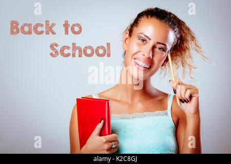 Beautiful smiling teenage girl with red book, thinking and looking at camera. Stock Photo