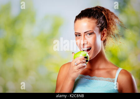Smiling young woman with braces on white teeth holding green apple and looking at camera. Stock Photo