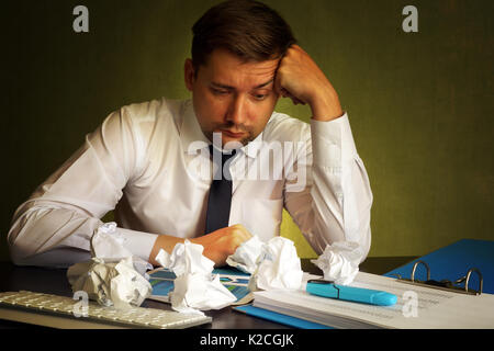 Frustrated businessman looking on a financial report and crumpled paper. Stock Photo