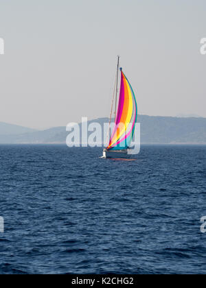 a yacht boat multicoloured multicolored sail with mountains in background  clear blue sky calm water sea ocean Stock Photo