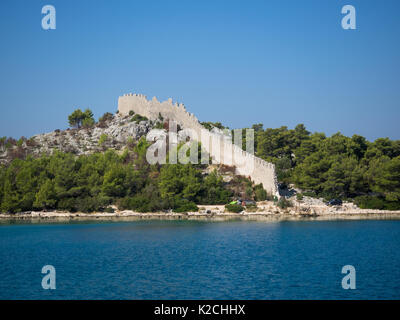 a view of an ancient wall ruins with battlements and ramparts surrounded by forest and trees on the Croatian coastline with clear blue sky, Luka, Uval Stock Photo