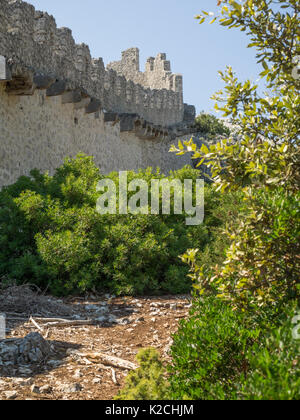 a view of an ancient stone wall ruins with battlements and ramparts surrounded by woods forest trees Croatian coastline clear blue sky Stock Photo