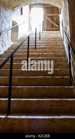 a view up dark stone stairs staircase towards an open wooden door with bright light shaft shining through at the top Stock Photo