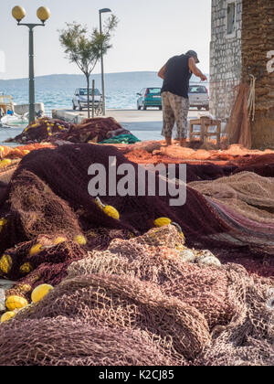 a fisherman standing sewing mending repairing his fishing net nets with a needle and thread on the quayside by the sea, Croatia Stock Photo