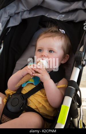 10 month old baby girl enjoying an ice-cream while sitting in her buggy. Stock Photo