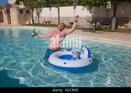 A drunk father on holiday with his toddler in a swimming pool. Stock Photo