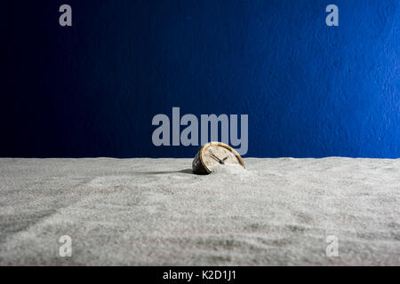 Abstraction: An ancient alarm clock buried in white sand on a blue background and fog Stock Photo