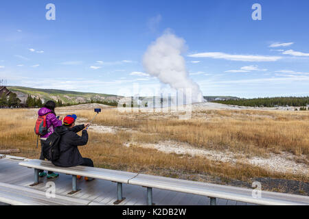 Tourists watching Old Faithful Geyser in Upper Geyser Basin, Yellowstone National Park, Wyoming, USA. September 2015. Stock Photo