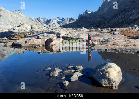 Woman hiker walking round mountain lake in Titcomb Basin in Wind River Range of Bridger Wilderness, Bridger National Forest, Wyoming, USA. September 2015. Model released Stock Photo